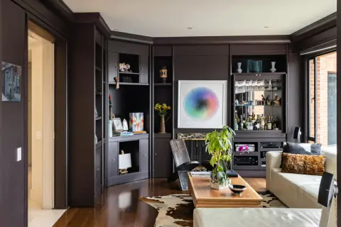 Dark floors can make a room feel cozy, not smaller. This living room features dark wood floors, a built-in bar, and a colorful art piece.