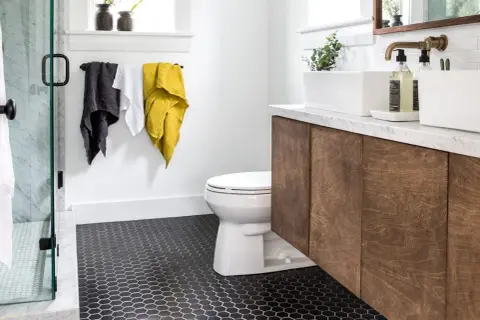 Modern bathroom with dark hexagonal tile floor, a classic choice for types of bathroom floor, a white toilet, and a wooden vanity.