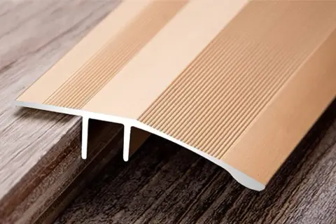 A metallic transition strip bridges two different wood-look floors, one lighter and one darker, showcasing the seamless finish of cut vinyl flooring.