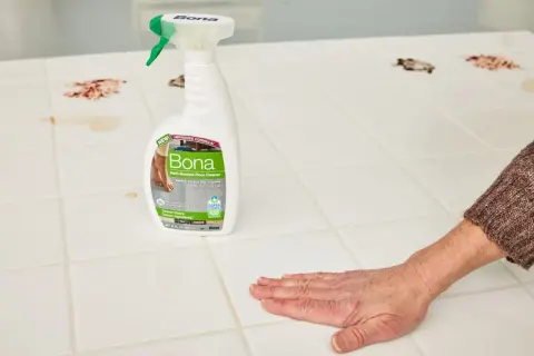 A hand wipes a stained porcelain floor tile with Bona Hard-Surface Floor Cleaner, showcasing effective porcelain floor tile cleaners.