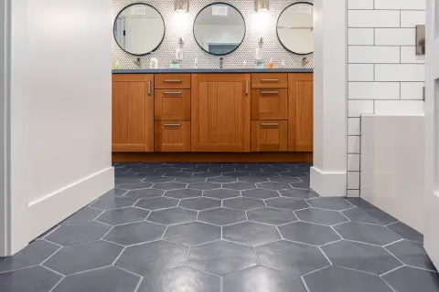 Hexagonal floor tiles create a dynamic pattern, giving the illusion of a larger space. A wooden vanity with three circular mirrors sits above.