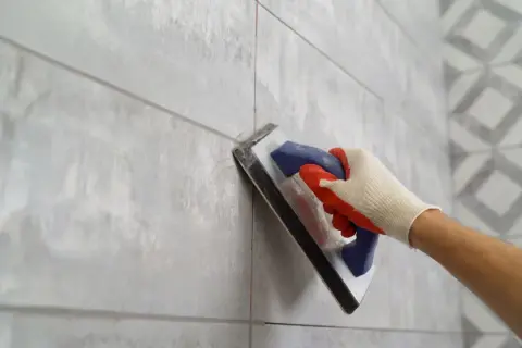 Gloved hand applies grout to a tiled wall, ensuring the best grout for shower floor longevity.