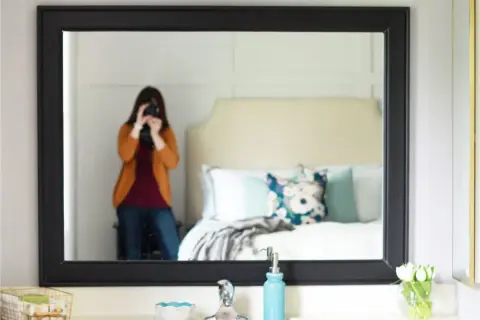 A person takes a selfie in a mirror with a black frame, showcasing a bedroom and a DIY mirror frame project.