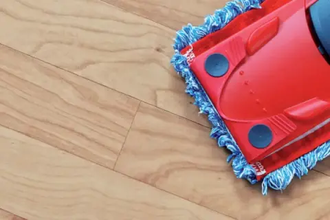 A red mop with blue fringe is cleaning a light wood-look vinyl floor, leaving it spotless.