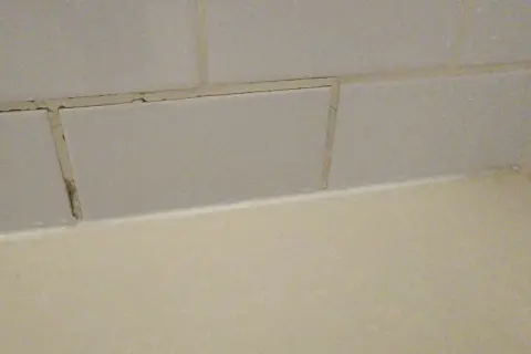 Cracked grout lines between light grey tiles suggest a need for repair. The question is, can you grout over grout?