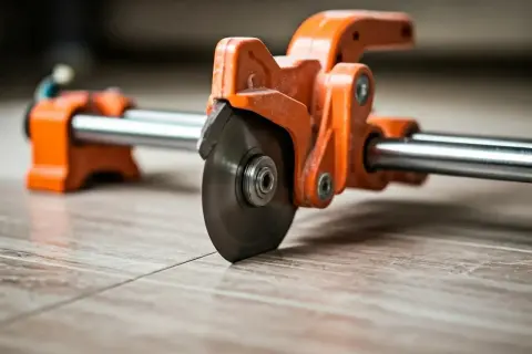 An orange tile cutter with a spinning blade is positioned on a tiled floor, ready to make a precise cut. This shows how to use a tile cutter for a clean finish.