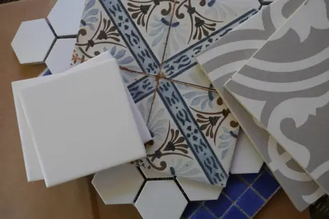 A collection of assorted tiles, including white hexagons, patterned squares, and grey wavy tiles, perfect for DIY leftover tile ideas.