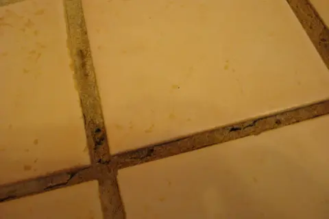 Close-up of beige tiles with visible grout cracking in a shower, showing signs of wear and tear.