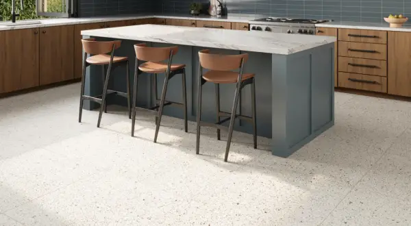 A modern kitchen with a blue island, wooden cabinets, and a beautiful bella terrazzo floor. Three bar stools are pulled up to the island.