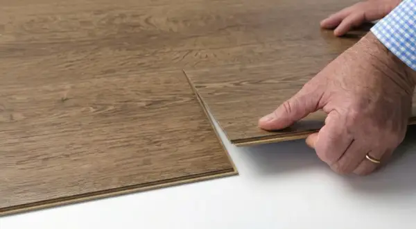 Hands demonstrate how to replace vinyl plank flooring by clicking a new plank into place.