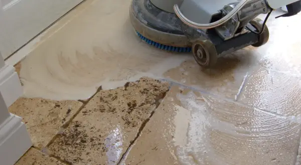 A floor buffer machine is used to clean travertine tile, creating suds and removing dirt.