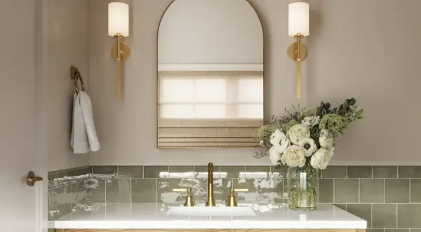 Elegant bathroom vanity with brass fixtures, a large arched mirror, and wall sconces that cast light up and down. A bouquet of white flowers adds a touch of luxury.