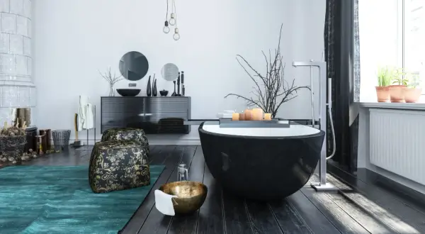 Modern bathroom with a black freestanding tub, dark wood floors, and a teal rug.