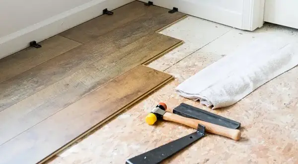 Tools for installing LVT flooring, including a rubber mallet and pry bar, are laid out next to planks being fitted.