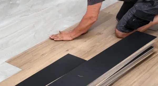 A person is installing vinyl plank flooring, carefully laying down a plank on a prepared surface.