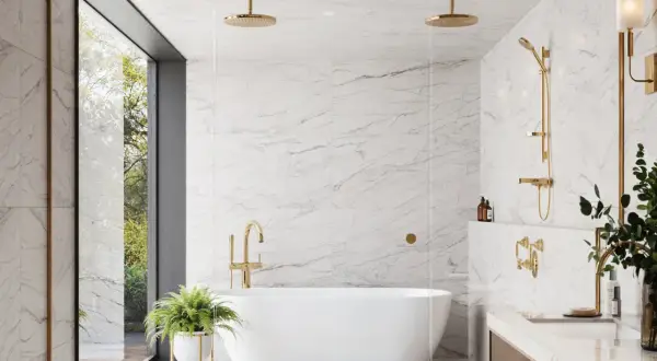 A luxurious bathroom featuring white marble tile with light grey grout, a freestanding tub, and gold fixtures.