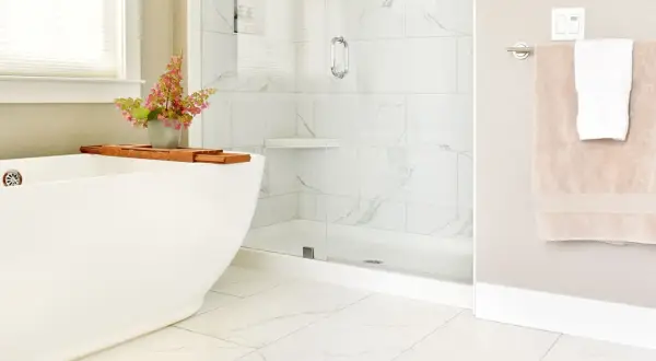 A modern bathroom with white marble tiles and a subtle marble tile grout color. A freestanding tub and glass shower create a spa-like feel.