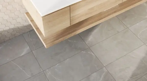 A modern bathroom vanity with wood grain drawers sits above large format tile flooring. The grout lines are thin, emphasizing the size of the tiles.