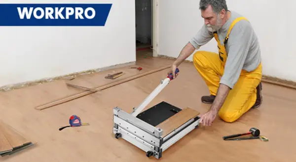 Man in yellow overalls uses a WORKPRO flooring cutter to demonstrate how to cut flooring. Tools and planks are nearby.