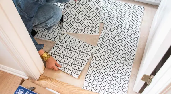 A person is laying down black and white patterned peel and stick floor tiles. No grout is needed for these tiles.