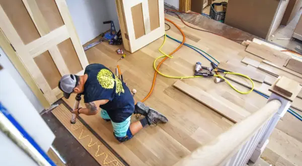 A worker applies adhesive to planks, demonstrating how to install luxury vinyl tile. Tools and materials are nearby.