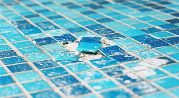 Close-up of a damaged mosaic tile surface, showing loose blue glass tiles. This image highlights the need to install glass mosaic tiles carefully.