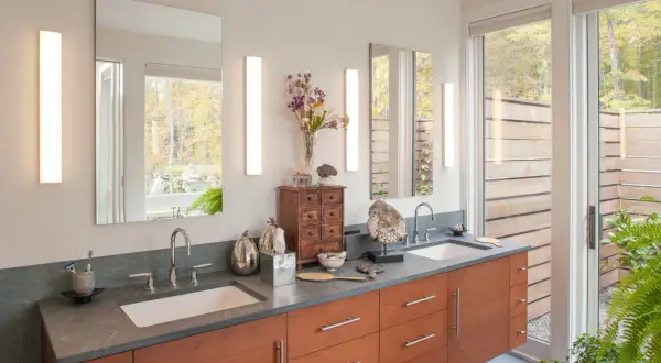 Modern bathroom vanity with two vertical lights over the sinks, reflecting a serene forest view.