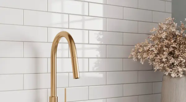 A gold faucet and dried flowers complement a white subway tile backsplash, showcasing a clean look after learning how to grout subway tile.