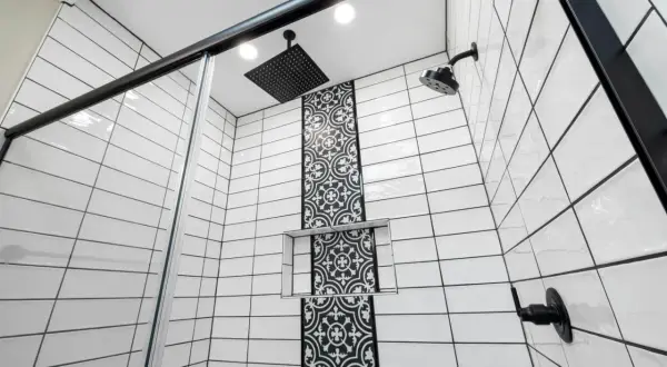 Modern shower with white subway tiles and black grout, featuring a decorative black tile accent and black fixtures.