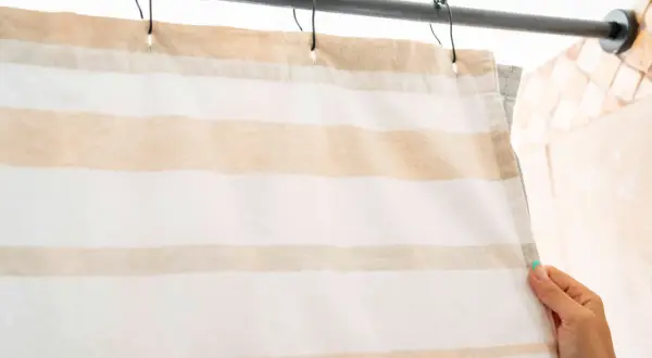 A hand holds a striped shower curtain hanging from a rod.