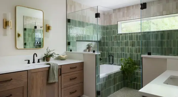 A modern bathroom features a soaking tub surrounded by glossy green and beige modern bathroom tiles, a glass shower enclosure, and a wooden vanity.