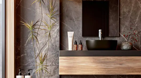 Modern bathroom vanity ideas featuring a floating wood shelf, dark vessel sink, and marble walls. A tall plant adds a natural touch.