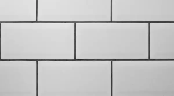 A clean, modern wall features rows of white tile with thin, dark grey grout lines, creating a classic subway tile pattern.