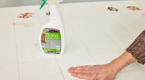 A hand wipes a stained porcelain floor tile with Bona Hard-Surface Floor Cleaner, showcasing effective porcelain floor tile cleaners.