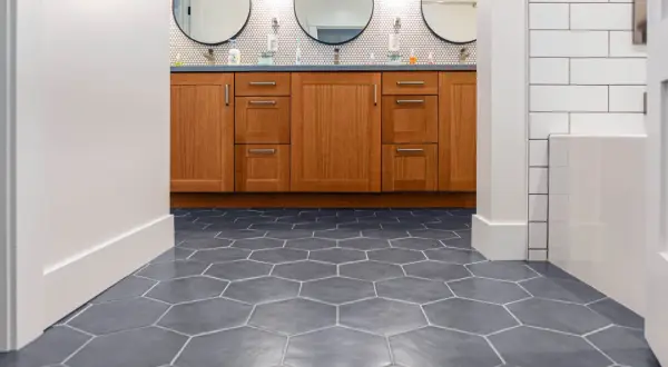 Hexagonal floor tiles create a dynamic pattern, giving the illusion of a larger space. A wooden vanity with three circular mirrors sits above.