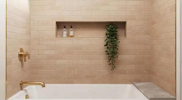A modern bathroom with a random subway tile pattern in a warm, peachy hue. A gold faucet and shower controls complement the tiles.