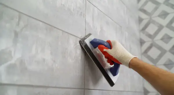 Gloved hand applies grout to a tiled wall, ensuring the best grout for shower floor longevity.