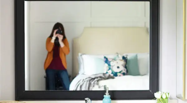 A person takes a selfie in a mirror with a black frame, showcasing a bedroom and a DIY mirror frame project.