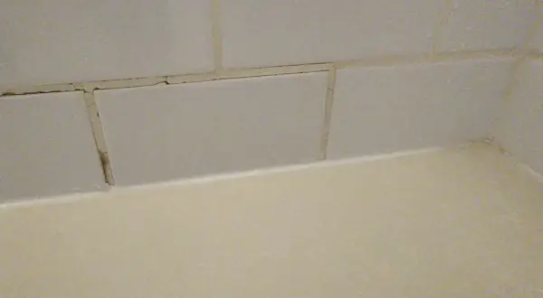 Cracked grout lines between light grey tiles suggest a need for repair. The question is, can you grout over grout?