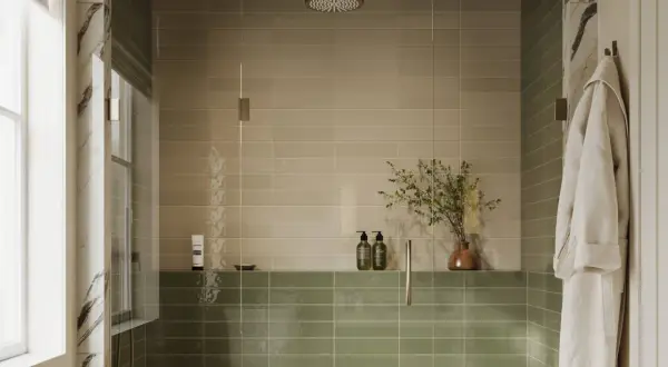 A modern shower with two-toned, low maintenance shower tile in beige and sage green. A glass enclosure, rainfall showerhead, and a plush robe complete the serene space.