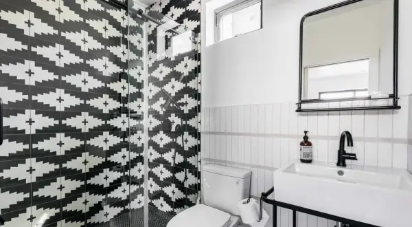 A modern bathroom with a striking black and white tile texture on the shower walls. The geometric pattern creates a bold statement.