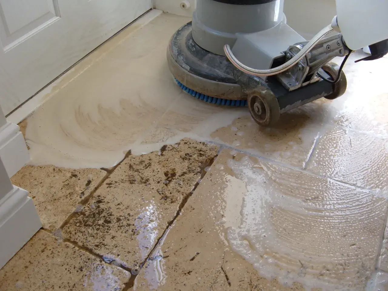 A floor buffer machine is used to clean travertine tile, creating suds and removing dirt.