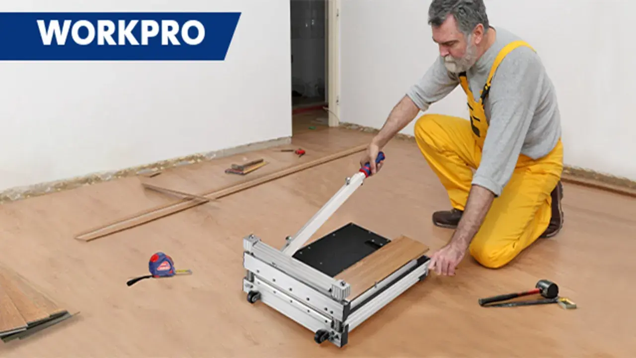 Man in yellow overalls uses a WORKPRO flooring cutter to demonstrate how to cut flooring. Tools and planks are nearby.
