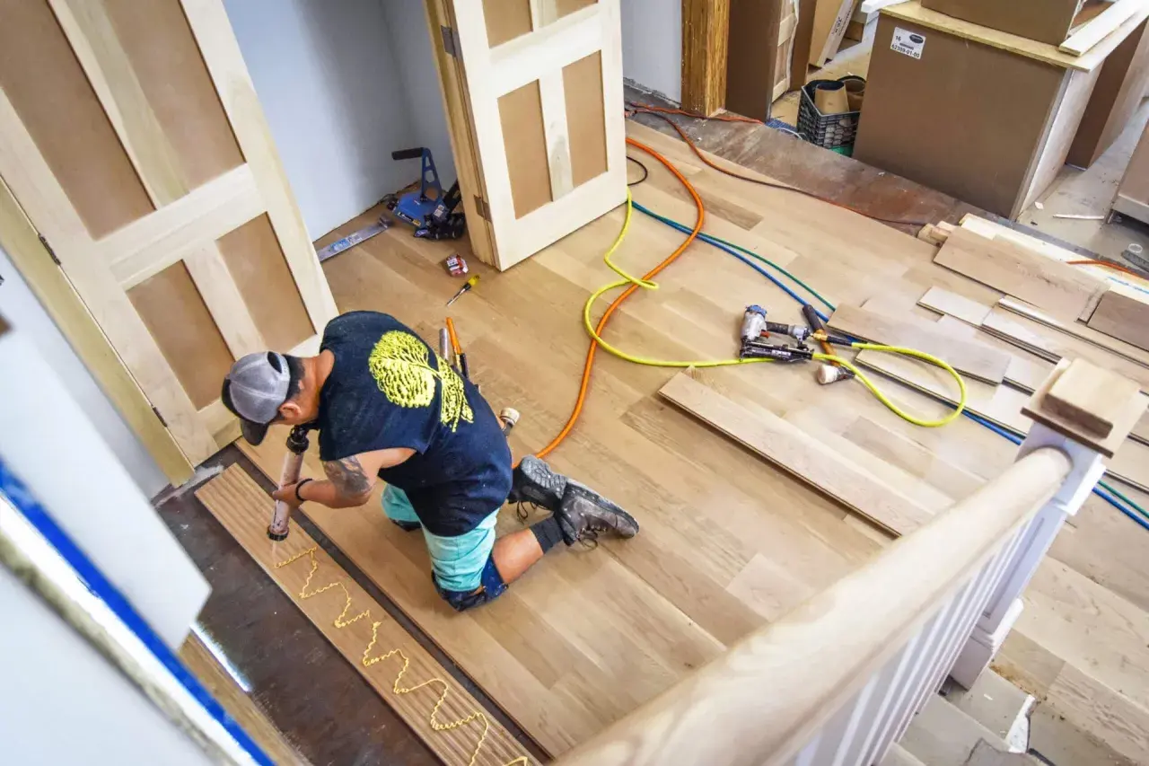 A worker applies adhesive to planks, demonstrating how to install luxury vinyl tile. Tools and materials are nearby.