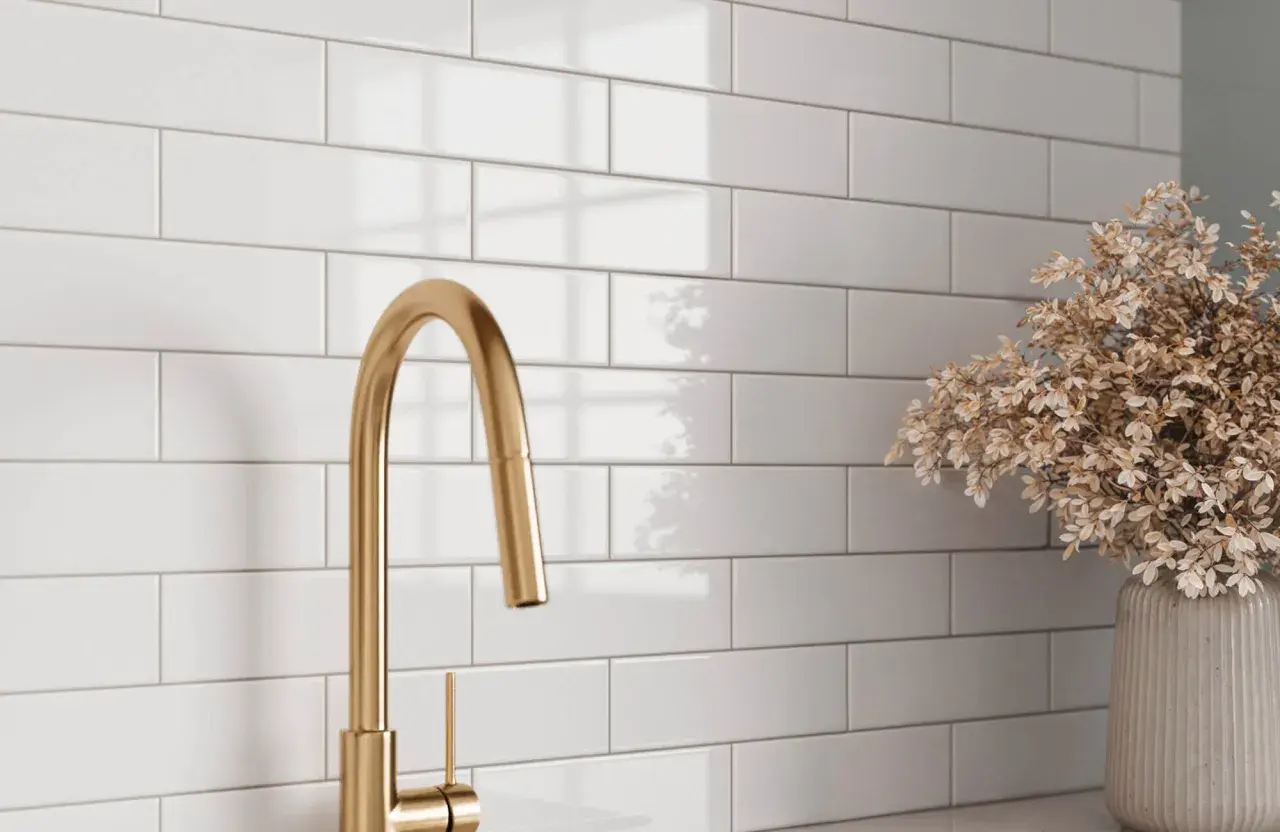 A gold faucet and dried flowers complement a white subway tile backsplash, showcasing a clean look after learning how to grout subway tile.