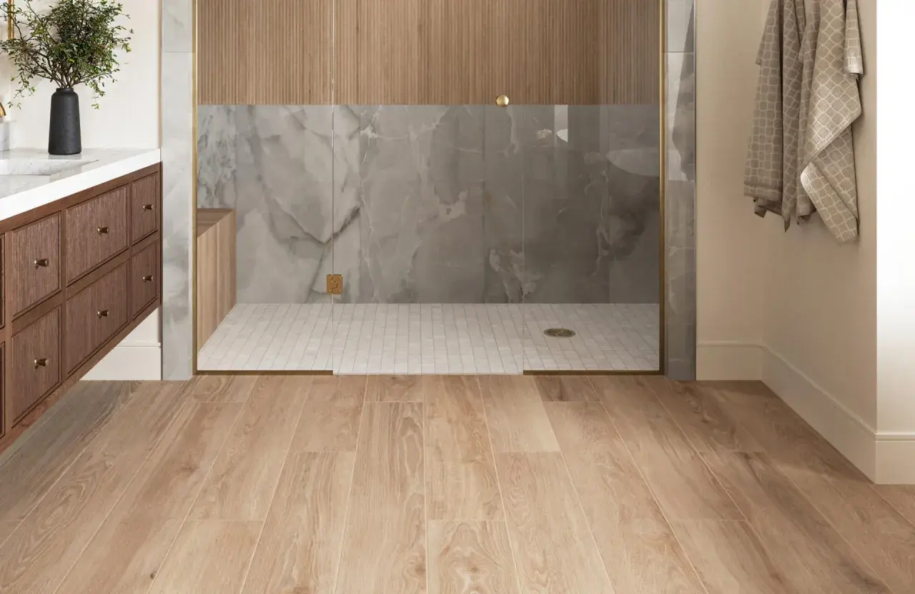 Modern bathroom with wood-look porcelain tile flooring. The shower features marble-look tile and wood accents. Considering porcelain wood tile pros and cons for your next renovation?