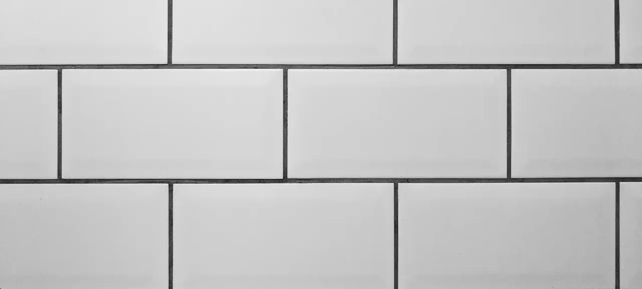 A clean, modern wall features rows of white tile with thin, dark grey grout lines, creating a classic subway tile pattern.