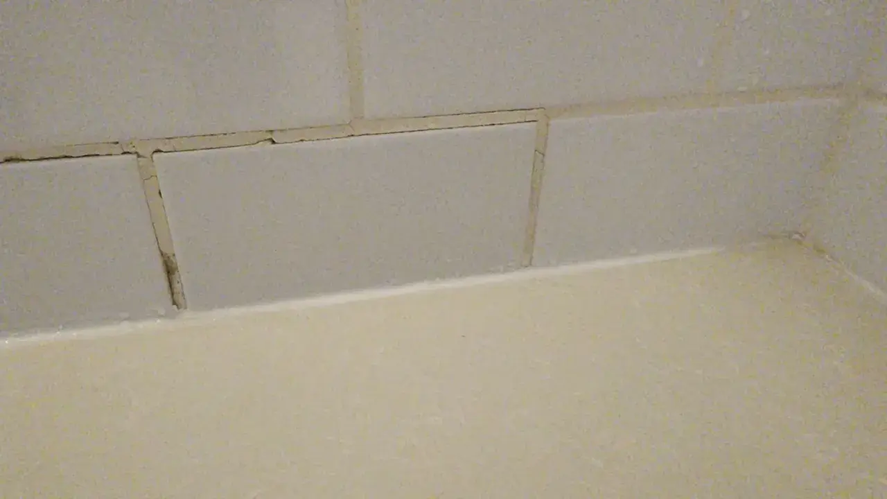 Cracked grout lines between light grey tiles suggest a need for repair. The question is, can you grout over grout?