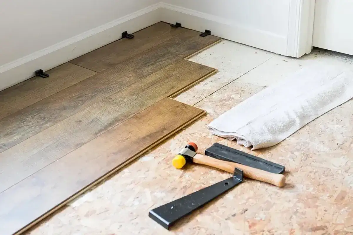 Tools for installing LVT flooring, including a rubber mallet and pry bar, are laid out next to planks being fitted.