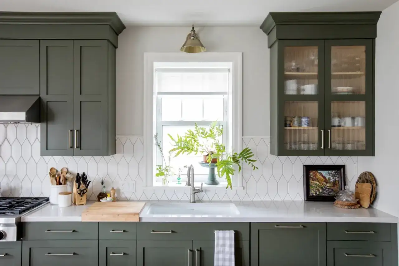 A modern kitchen features dark green cabinets and a white picket tile backsplash arranged in a vertical pattern.